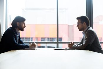 Two Men Sitting Across From Each Other At A Table.